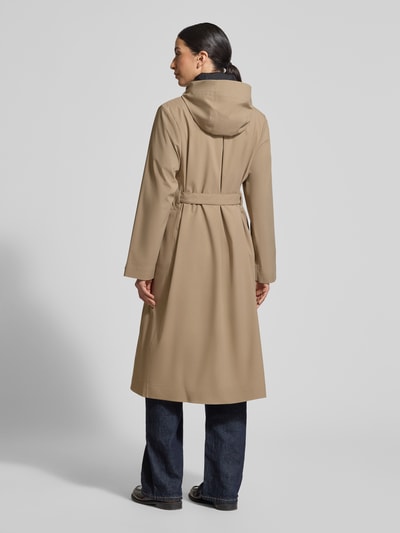 Frauenmodel trägt Regular Fit Mantel mit Stehkragen Modell 'Suva' von Rains in Beige, taillierte Passform, Pattentaschen, Ganzkörperansicht Rückansicht. Rückenlänge bei Größe S: 113 cm, Schulterbreite: 42 cm, Brustweite: 51 cm, Ärmellänge: 62 cm, abnehmbares Stoffband.