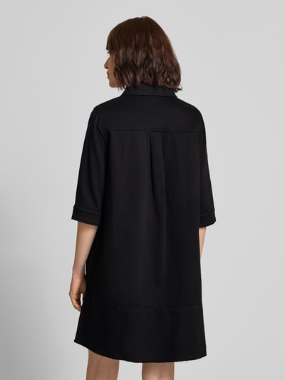 Frauenmodel trägt knielanges Hemdblusenkleid mit Knopfleiste und 1/2-Arm von Marc Cain in Schwarz mit geradem Schnitt, Rückansicht, Ganzkörperansicht Rückansicht. Rückenlänge bei Größe 36: 89 cm, Brustweite: 52 cm, Ärmellänge: 31 cm, Hemdblusenkragen.
