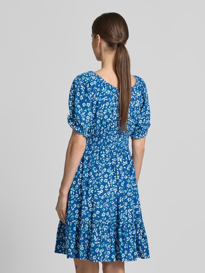 Frauenmodel trägt Minikleid aus Viskose mit Kordelzug und Quasten von Apricot, blaues Blumenmuster, Taillierter Schnitt, Ganzkörperansicht Rückansicht. Rückenlänge bei Größe S: 82 cm, Brustweite bei Größe S: 34 cm, Ärmellänge bei Größe S: 21 cm, Rundhalsausschnitt mit Rüschen, Rüschenärmel, Smok-Detail.