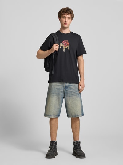 Mannelijk model draagt t-shirt met motiefprint Model 'DONKEY TAXI' van The North Face, puur katoen, regular fit, ronde hals, ruglengte maat M 70 cm, zwarte tinten, lichte printaccenten, denim short, laarzen, ganse lichaamsfoto van voren.