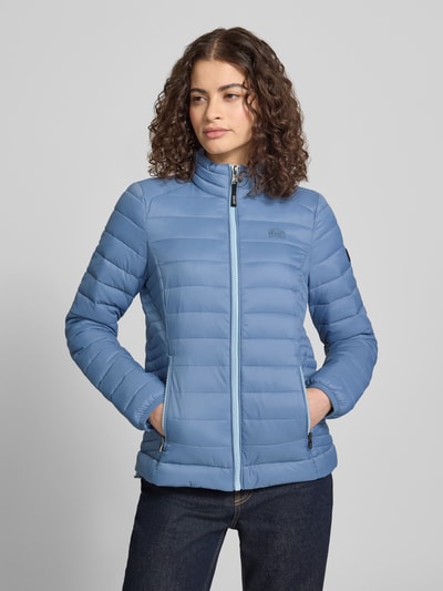 Modelka kobieca ma na sobie niebieską Steppjacke mit Logo-Stitching Modell 'FUJI' od Superdry, prosty krój, stójka, boczne kieszenie na zamek, zamek błyskawiczny, miękka tekstura, Szerokość w rozmiarze S: 50 cm, długość tyłu: 62 cm, długość rękawa: 69 cm, Szerokość w ramionach: 40 cm; zdjęcie: widok całej sylwetki z przodu.