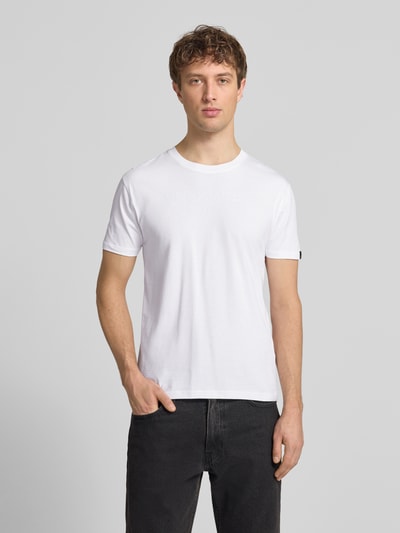 Männermodel trägt T-Shirt aus Baumwolle von Alpha Industries, Weiß, Gerader-Schnitt, Rundhalsausschnitt, Label-Print-Details, Rückenlänge 68 cm, Ganzkörperansicht von vorne.
