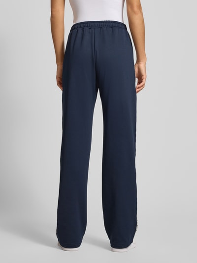 Männermodel trägt Sportliche Trackhose mit geradem Bein von REVIEW in dunkelblau mit koronkowe elementy, zaszewka z przodu, wyhaftowane logo na bocznej kieszeni, długość wewnętrzna nogawki w rozmiarze S: 39 cm, ganzkörperansicht rückansicht.