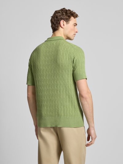 Männermodel trägt Slim Fit Kurzarm Pullover mit Kaschmir-Anteil in Strick-Optik von FTC-Cashmere in Grün, Rückansicht, Ganzkörperansicht.