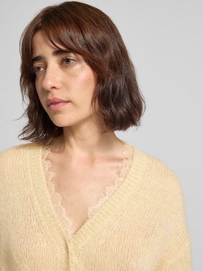 Modelka nosi kardigan rozpinany 'Strickjacke mit V-Ausschnitt und Spitzenbesatz' von Luisa Cerano, Mieszanka materiałów z domieszką alpaki, krój relaxed fit, dekolt w serek, obszycie koronką, listwa guzikowa, Długość tyłu w rozmiarze 36: 59 cm, Długość rękawów w rozmiarze 36: 44 cm, jasny odcień, delikatna tekstura dzianiny, zbliżenie na górną część ciała, widok z przodu