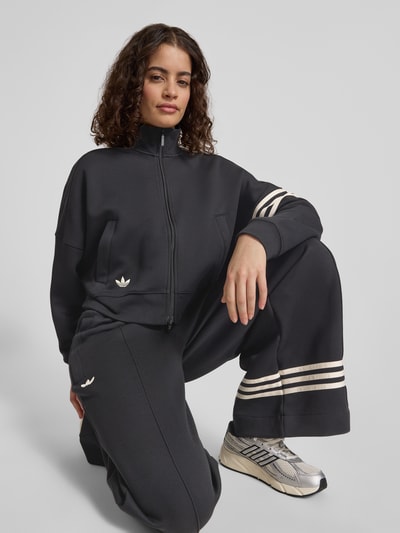 Modelka nosi Regular Fit Sweatjacke aus Baumwoll-Mix od adidas Originals, gładka czerń, logo, zamek, długie rękawy, bawełna, widok z przodu, ujęcie całej sylwetki.