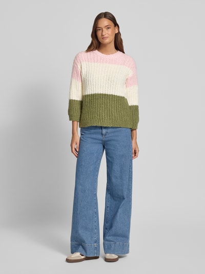 Frauenmodel trägt Strickpullover mit Rundhalsausschnitt von More & More im Grobstrick, Material-Mix mit Baumwoll-Anteil, Relaxed-Fit, breite Blockstreifen in Rosa, Weiß und Oliv, Rückenlänge Größe 36: 55 cm, Ärmellänge 48 cm, Ganzkörperansicht von vorne.
