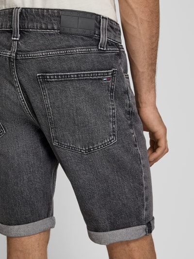 Männermodel trägt Regular Fit Jeansshorts aus bawełniany mieszanka von Tommy Jeans w stylizowana na denim z 5 kieszeni, naszywka z logo, wyhaftowane logo, szlufki na pasek, zapięcie na guzik i ukryty zamek błyskawiczny, widoczne szwy, ciemnoszary kolor, gładka tekstura, mieszanka bawełny, Ganzkörperansicht Rückansicht.