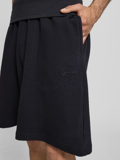 Männermodel trägt Regular Fit Shorts mit elastischem Bund von KARL KANI aus Reiner Baumwolle mit Strukturmuster, Nahaufnahme Oberschenkel.