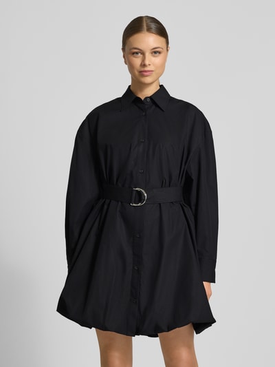 Frauenmodel trägt Tailliertes Hemdblusenkleid aus reiner Baumwolle Modell 'KUMIRA' von HUGO, unifarben schwarz, Mini-Länge, Knopfleiste, Gürtel, langarm, elastischer Saum, Ganzkörperansicht von vorne.