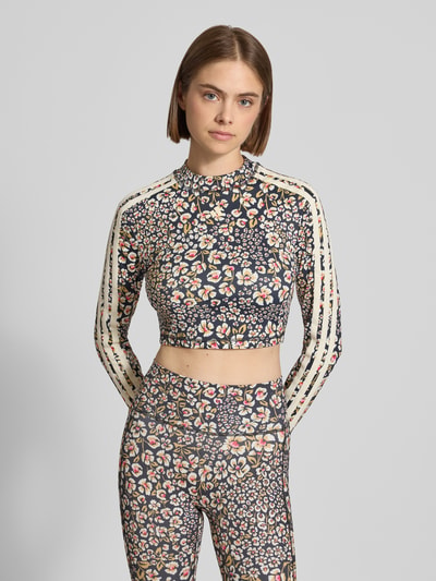 Frauenmodel trägt Slim Fit Sport-Top mit floralem Muster von adidas, dunkle Grundfarbe mit buntem Blumenprint, adidas Sportswear, Nahaufnahme Oberkörper