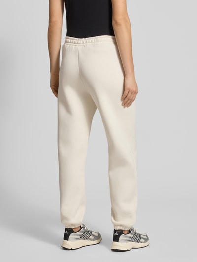 Frauenmodel trägt Basic Sweatpant mit Bündchen am Saum und Seitentaschen von Review, Baumwoll-Mix, lockere Passform, Logo-Stickerei, Ganzkörperansicht Rückansicht.