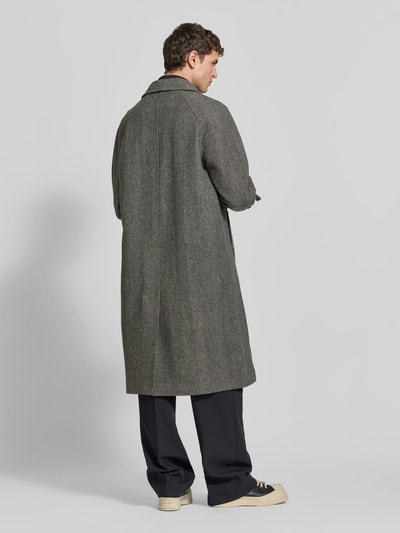 Männermodel trägt Wollmantel aus reiner Wolle von Forét, lockere Passform, Umlegekragen, abgedeckte Knopfleiste, Ärmelriegel, grauer Farbton, Rückenlänge 118 cm, Schulterbreite 45 cm, Ärmellänge 68 cm, strukturierte Oberfläche, Ganzkörperansicht Rückansicht