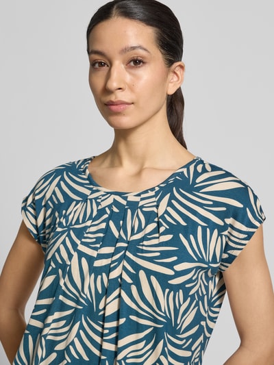 Frauenmodel trägt Regular Fit Bluse aus Viskose-Mix Modell 'Minou' von ZABAIONE, floraler Allover-Print in Blau und Beige, Kurzärmelig, Rundhalsausschnitt, Elastischer Bund, Nahaufnahme Oberkörper.