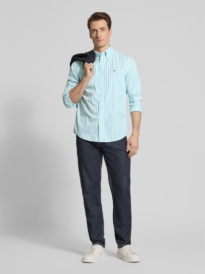 Männermodel trägt Regular Fit Freizeithemd aus Baumwoll-Popeline von Tommy Hilfiger mit türkis-weißem Streifenmuster, Ganzkörperansicht von vorne.