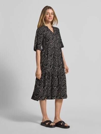 Frauenmodel trägt Ausgestelltes Maxikleid aus reiner Viskose Modell 'EASY JOY' von Vero Moda mit Allover-Muster, Henley-Ausschnitt, kurze Knopfleiste, halblange Ärmel, Maxi-Länge, schwarze und weiße Farben, lockere Passform, Ganzkörperansicht von vorne.