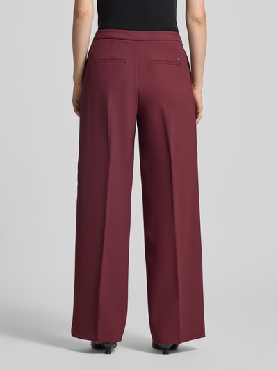 Frauenmodel trägt Wide Fit Hose mit Bügelfalten Modell 'Leya' von MOS MOSH in Bordeauxrot, glatte Textur, Ganzkörperansicht Rückansicht, Damen Hose von MOS MOSH, Bügelfalten, Haken- und Reißverschluss, Bundweite bei Größe 36: 62 cm, Innenbeinlänge bei Größe 36: 80 cm.