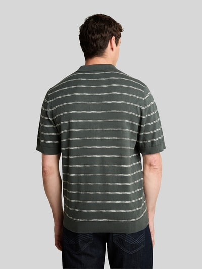 Männermodel trägt Regular Fit Poloshirt aus reiner Baumwolle von Tom Tailor in Dunkelgrün mit weißen Streifen, Ganzkörperansicht Rückansicht.