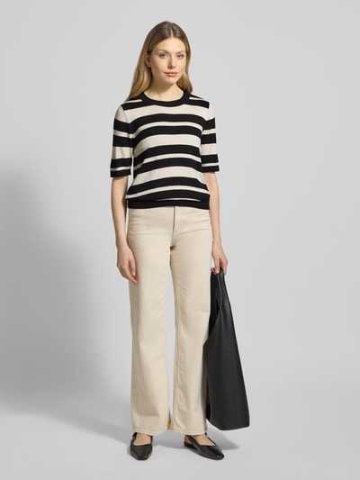 Frauenmodel trägt Strickshirt mit Rundhalsausschnitt und Label-Detail von More & More, Streifenmuster in Schwarz und Beige, Viskose-Elasthan-Mix, Regular Fit, kombiniert mit heller Hose, Ganzkörperansicht von vorne.