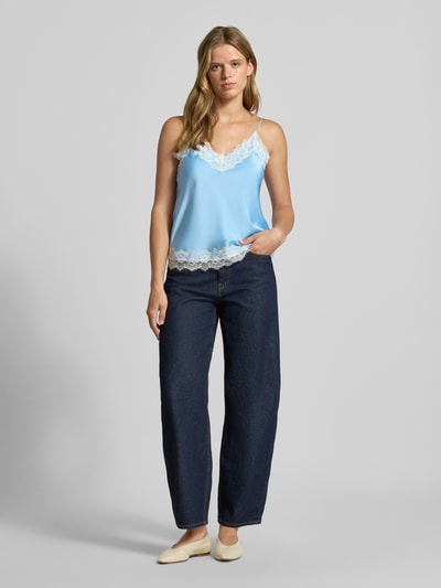 Frauenmodel trägt Regular Fit Top aus Satin mit Spitzenbesatz von REVIEW in Hellblau, kombiniert mit dunkler Hose, Ganzkörperansicht von vorne, Damen Top aus Satin, Spaghetti-Träger, Rückenlänge bei Größe S: 39 cm.