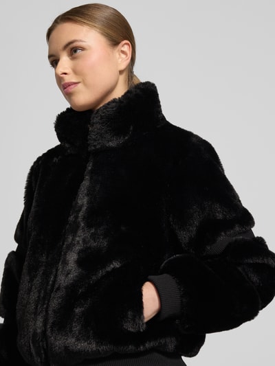 Frauenmodel trägt Jacke mit Teddyfell und gerippten Abschlüssen von Guess in Schwarz mit Stehkragen und Reißverschluss, Nahaufnahme Oberkörper, Kontext: Damen Jacke, gerader Schnitt, Rückenlänge 56 cm, Schulterbreite 38 cm, Brustweite 53 cm, Ärmellänge 61 cm.