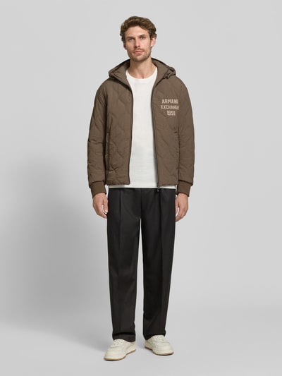 Männermodel trägt Jacke mit Steppnähten und Label-Detail von Armani Exchange in Braun mit Kapuze, Zweiwege-Reißverschluss, Eingrifftaschen, Regular Fit, Ganzkörperansicht von vorne.