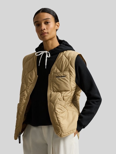 Mannelijk model draagt Regular Fit Steppweste met borstzak van Polo Ralph Lauren in effen beige met label stitching, v-hals, doorgestikte textuur, vooraanzicht van het bovenlichaam.