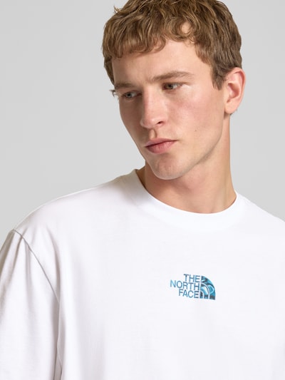 Męski model nosi Oversized T-Shirt mit Logo und Rundhalsausschnitt od The North Face z białej bawełny, oversize, logo, dekolt okrągły, długość tyłu w rozmiarze M: 73 cm, zbliżenie na górną część ciała