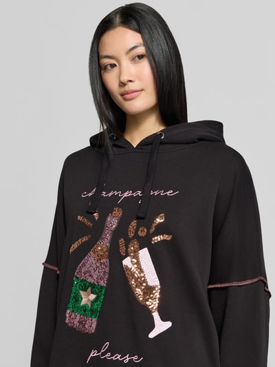 Frauenmodel trägt schwarzen Hoodie aus reiner Baumwolle von miss goodlife mit Pailletten-Besatz, lockerer Passform, Nahaufnahme Oberkörper.