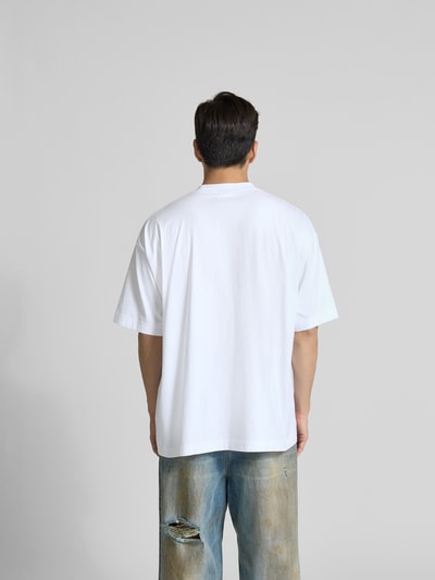 Männermodel trägt Oversized T-Shirt aus reiner Baumwolle von VETEMENTS, Weiß, Stehkragen, Label-Stitching, Rückenlänge 78 cm, Ganzkörperansicht Rückansicht.