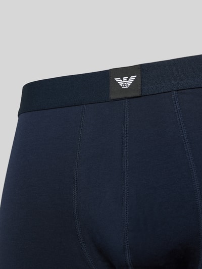 Männermodel trägt Trunks mit elastischem Logo-Bund im 3er-Pack von Emporio Armani aus Baumwoll-Elasthan-Mix, Nahaufnahme Rückansicht.