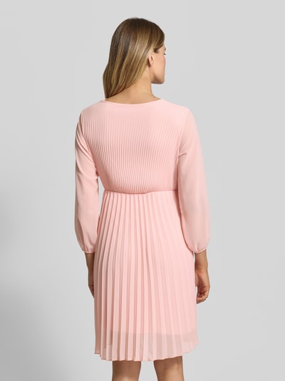 Frauenmodel trägt Knielanges Kleid mit Plisseefalten Modell 'Im44sa' von ZABAIONE in zartem Rosa, taillierter Schnitt, Rückansicht. Kontext: Damen Kleid von ZABAIONE, Taillierter Schnitt, Knielänge, Wickel-Optik, Plisseefalten, Rückenlänge bei Größe S: 90 cm, Brustweite bei Größe S: 38 cm, Ärmellänge bei Größe S: 52 cm.