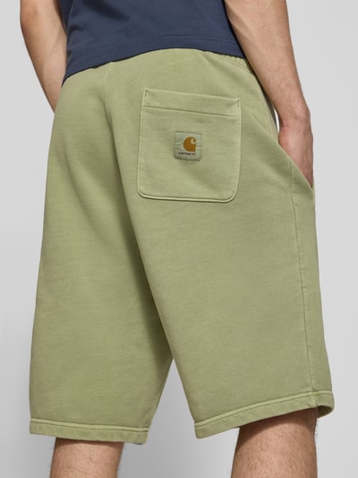 Männermodel trägt Sweatshorts mit Eingrifftaschen Modell 'Nelson' von Carhartt, grün, reine Baumwolle, Relaxed Fit, Ganzkörperansicht Rückansicht