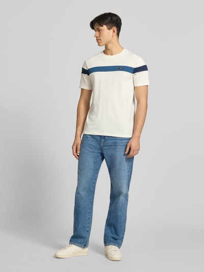 Männermodel trägt Regular Fit T-Shirt mit Logo-Detail Modell 'Caserio' von Ellesse in Creme mit dunkelblauen Streifen, Ganzkörperansicht von vorne