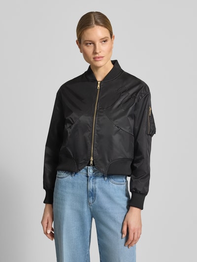 Kobiece modelka nosi bomberkę 'Bomberjacke mit Zweiwege-Reißverschluss' od Original Bombers, czarna, haft, kieszenie zapinane na zamek błyskawiczny, stójka, krój regular fit, długość tyłu w rozmiarze S: 55 cm, szerokość ramion w rozmiarze S: 50 cm, szerokość klatki piersiowej w rozmiarze S: 56 cm, długość rękawów w rozmiarze S: 64 cm, widok całej sylwetki z przodu.