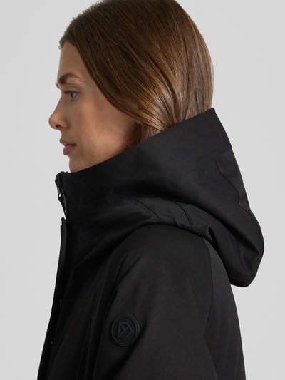 Frauenmodel trägt czarną parkę z kapturem z wypełnieniem Thermore Parka mit Kapuze und Thermore Füllung von Didriksons, wyhaftowane logo na ramieniu, wodoodporny, wiatroszczelny, oddychający, prosty krój, gładka tekstura, zamek błyskawiczny, rzep i guzik, boczne kieszenie z patkami, dzianinowe zakończenia rękawów, długość tyłu w rozmiarze 36: 102 cm, szerokość ramion w rozmiarze 36: 40 cm, szerokość w rozmiarze 36: 56 cm, długość rękawów w rozmiarze 36: 60 cm, zbliżenie na kaptur, Nahaufnahme Oberkörper.