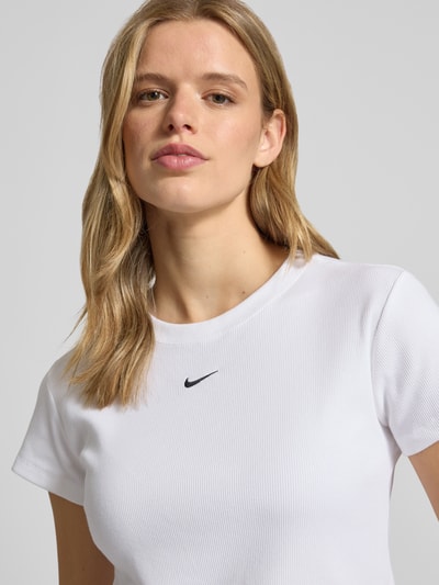 Frauenmodel trägt Cropped T-Shirt in Ripp-Optik mit Logo von Nike aus Baumwoll-Elasthan-Mix, Rundhalsausschnitt, Nahaufnahme Oberkörper.