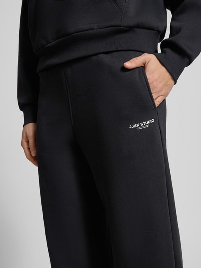 Męskimodel nosi High Waist Sweatpants mit elastischem Bund und Logo od JJXX z mieszanki bawełny, szerokie nogawki, logo, detailaufnahme.