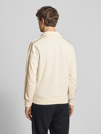 Männermodel trägt Slim Fit Sweatjacke mit Logo-Stitching Modell 'Niagara' von Jack & Jones in Beige mit schwarzen Details, Ganzkörperansicht Rückansicht. Rückenlänge 67 cm, elastische Abschlüsse, Eingrifftaschen und Stehkragen.