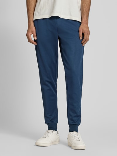 Männermodel trägt Sweatpants mit elastischem Bund Modell 'BERTONI' von Ellesse aus Baumwoll-Mix, Regular-Fit, Label-Detail, Ganzkörperansicht von vorne.