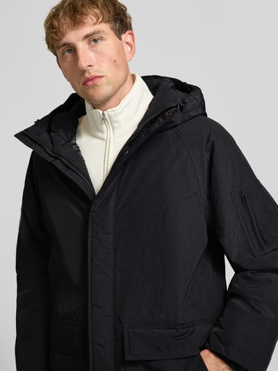 Männermodel trägt schwarzen Parka mit Pattentaschen Modell 'Stanwood' von Carhartt Work In Progress, Reißverschlussdetails, Nahaufnahme Oberkörper.