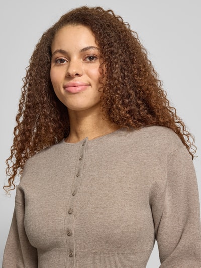 Modelka nosi Slim Fit Cardigan aus Viskose-Mix od Gina Tricot, krój regular fit, listwa guzikowa, okrągły dekolt, imitacja dzianiny, szerokie elastyczne wykończenia, kolor beżowy, długość tyłu 48 cm, długość rękawów 59 cm, mieszanka wiskozy, zbliżenie na górną część ciała
