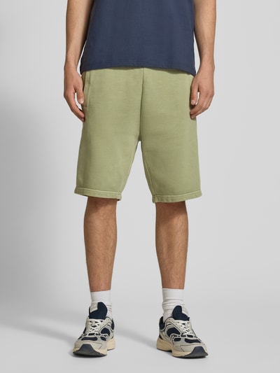 Männermodel trägt Sweatshorts mit Eingrifftaschen Modell 'Nelson' von Carhartt Work In Progress in Grün, Reine Baumwolle, Relaxed-Fit, Ganzkörperansicht von vorne.