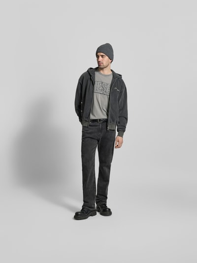 Männermodel trägt Regular Fit T-Shirt mit Logo-Detail von Diesel aus reiner Baumwolle, Rundhalsausschnitt, kurzärmelig, graue Töne, Ganzkörperansicht von vorne.