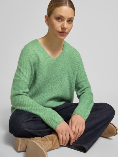 Frauenmodel trägt Strickpullover mit V-Ausschnitt Modell 'THORA' von MOS MOSH aus grünem Woll-Mix mit Alpaka-Anteil, Relaxed Fit, Ganzkörperansicht von vorne.