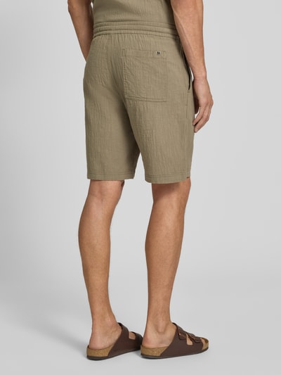 Männermodel trägt Relaxed Fit Stoffshorts aus einer katoen von s.Oliver RED LABEL in lichtbruin met zichtbare textuur, Ganzkörperansicht Rückansicht.
