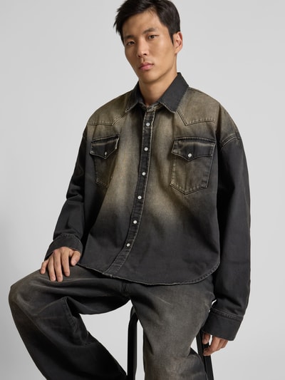 Männermodel trägt Relaxed Fit Jeanshemd im Used-Look von VETEMENTS aus Reine Baumwolle, schwarze Farbverläufe, Busttaschen, Langärmlig, Durchgehende Knopfleiste, Ganzkörperansicht von vorne.