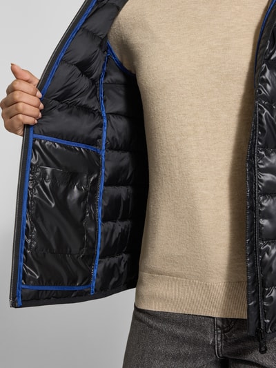 Frauenmodel trägt Jacke mit Kapuze von NAUTGÅRD in Schwarz mit blauen Nähten, lockerer Schnitt, Nahaufnahme Oberkörper.
