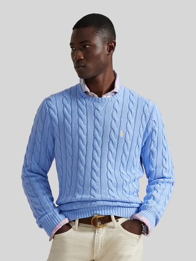 Männermodel trägt Regular Fit Strickpullover aus reiner Baumwolle von Polo Ralph Lauren in Hellblau, Zopfmuster, Logo-Detail, Ganzkörperansicht von vorne.