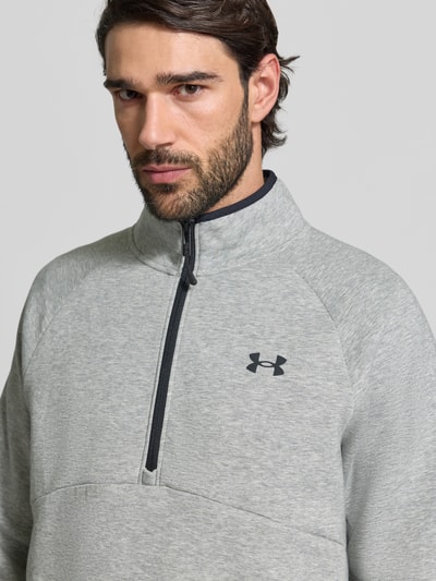 Männermodel trägt Regular Fit Pullover mit Logo-Print Modell 'Unstoppable' von Under Armour in Hellgrau mit Troyer-Kragen, Nahaufnahme Oberkörper.